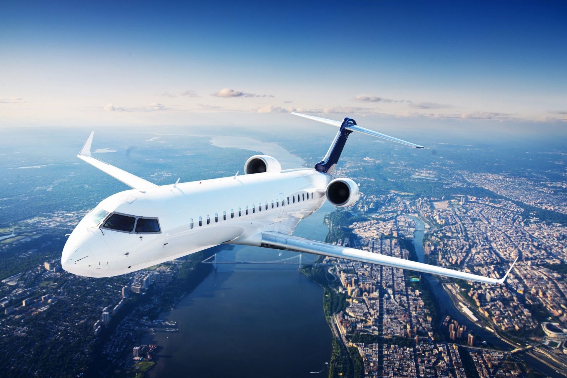 A White colored plane flying towards left over the sea and buildings